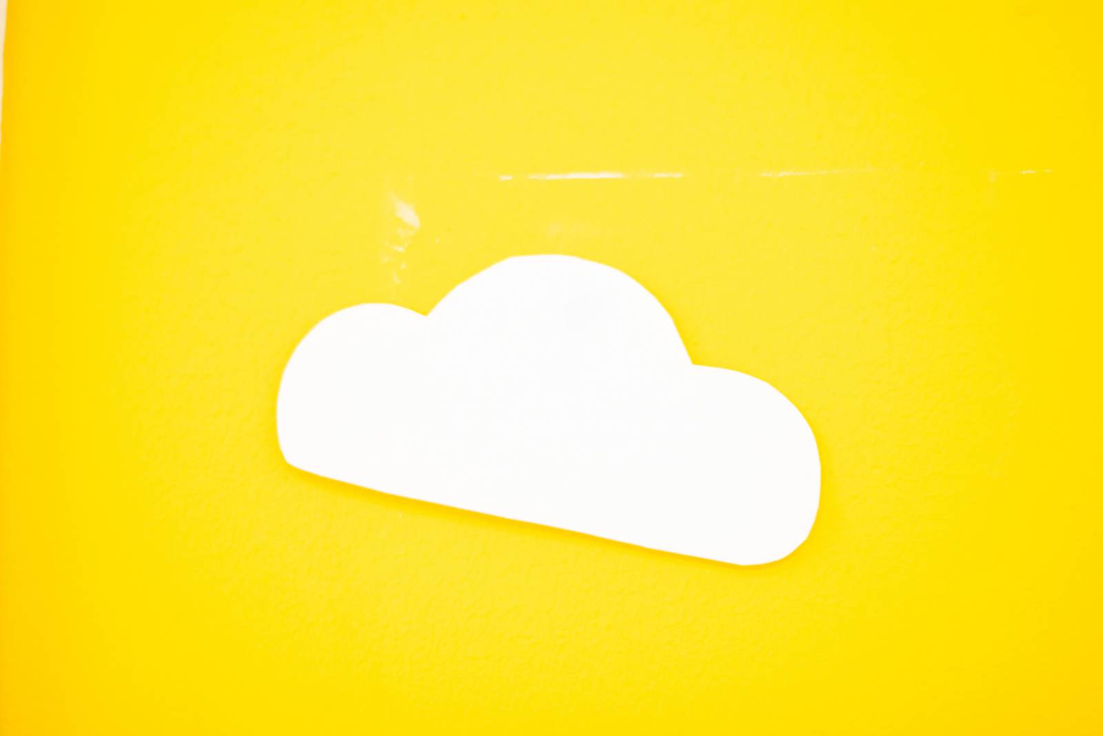 Kuvassa kirkkaan keltainen tausta, jolla yksi valkoinen, käsin piirretty pilvi.