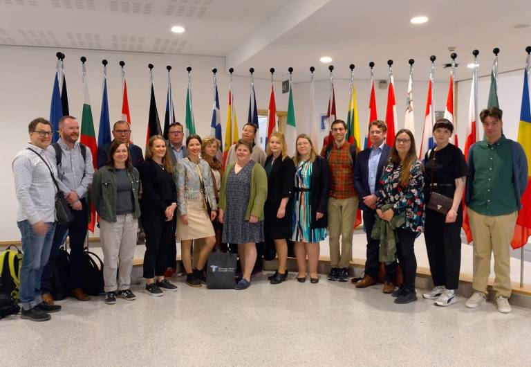 Group of 17 researchers from TAU standing before country flags in European Parliament.