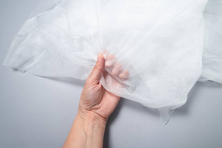A hand holding a white nonwoven fabric.
