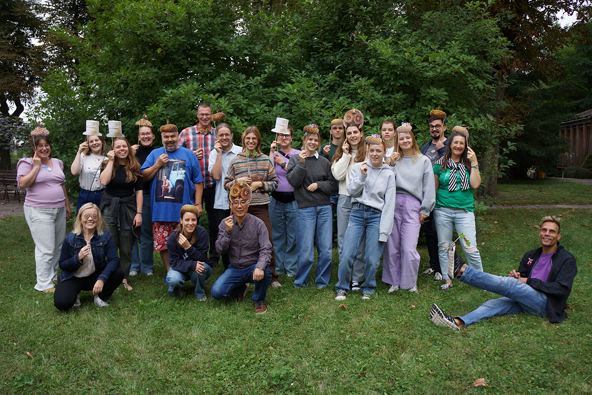 A big group of people outside on the grass, some wearing a mask.