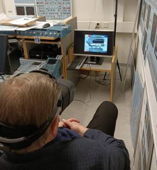 A man wearing XR glasses is sitting on a chair and watching a screen and a picture on it. 